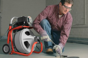 a plumber is using the drain snake to clear a clogged drain